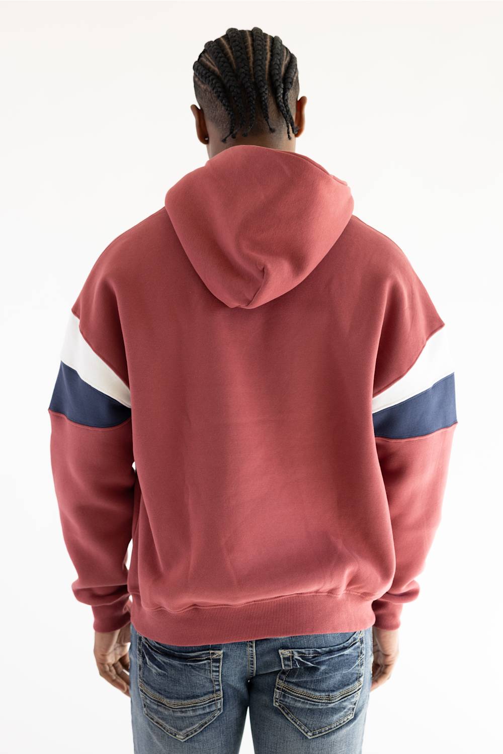 A person viewed from behind wearing a dusty rose hooded sweatshirt with white and navy blue color-blocked stripes on the sleeves, paired with blue jeans, against a plain white background.