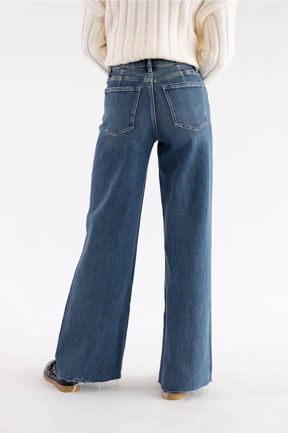 A person shown from the back wearing blue wide-leg jeans and a cream ribbed sweater, photographed against a clean white studio background.