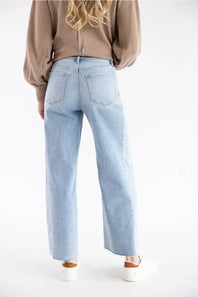 A person shown from the back wearing light-wash wide-leg denim jeans, a brown ribbed sweater, and white sneakers against a plain white studio background.
