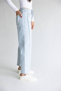 A model wearing light-wash blue denim jeans with vertical seam detailing, styled with a white long-sleeve top and white sneakers against a plain white studio background.