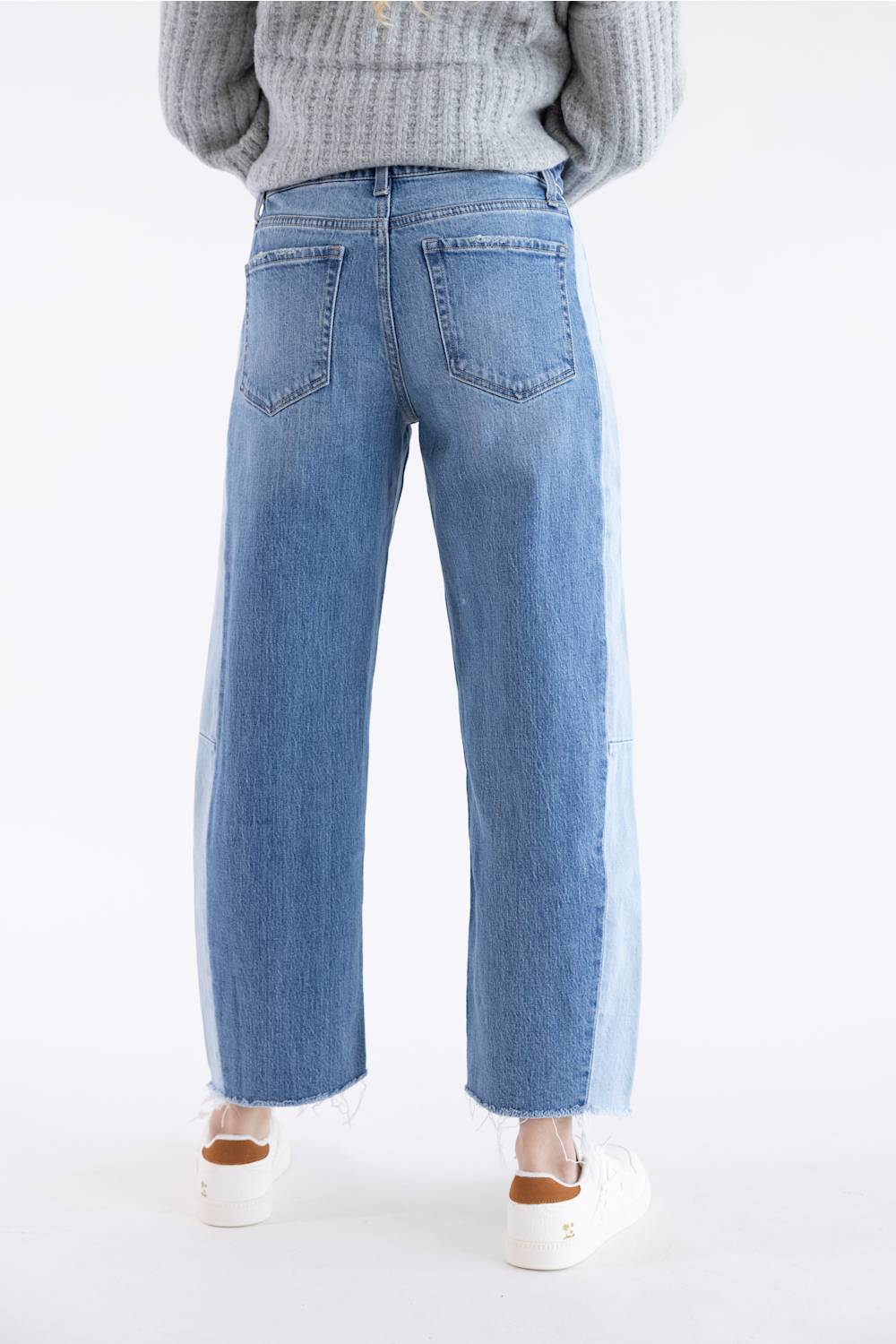 A person shown from the back wearing light-wash wide-leg denim jeans and a gray ribbed sweater against a plain white studio background.