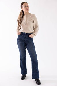 A woman modeling a beige knit sweater and dark blue straight-leg jeans against a plain white studio background.