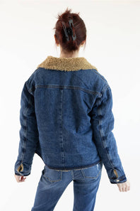 A person shown from the back wearing a blue denim jacket with a tan sherpa collar, paired with blue jeans, against a plain white background.