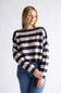 A woman wearing a navy blue and cream striped knit sweater with blue jeans, standing against a plain light gray studio background.