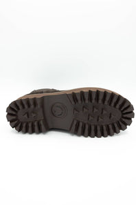 The rugged outsole of a brown boot, showing deep lugs and a circular embossed logo, photographed from underneath on a white background.