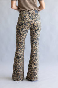 A person shown from the back wearing leopard-print flare pants and a taupe top against a light gray studio background.