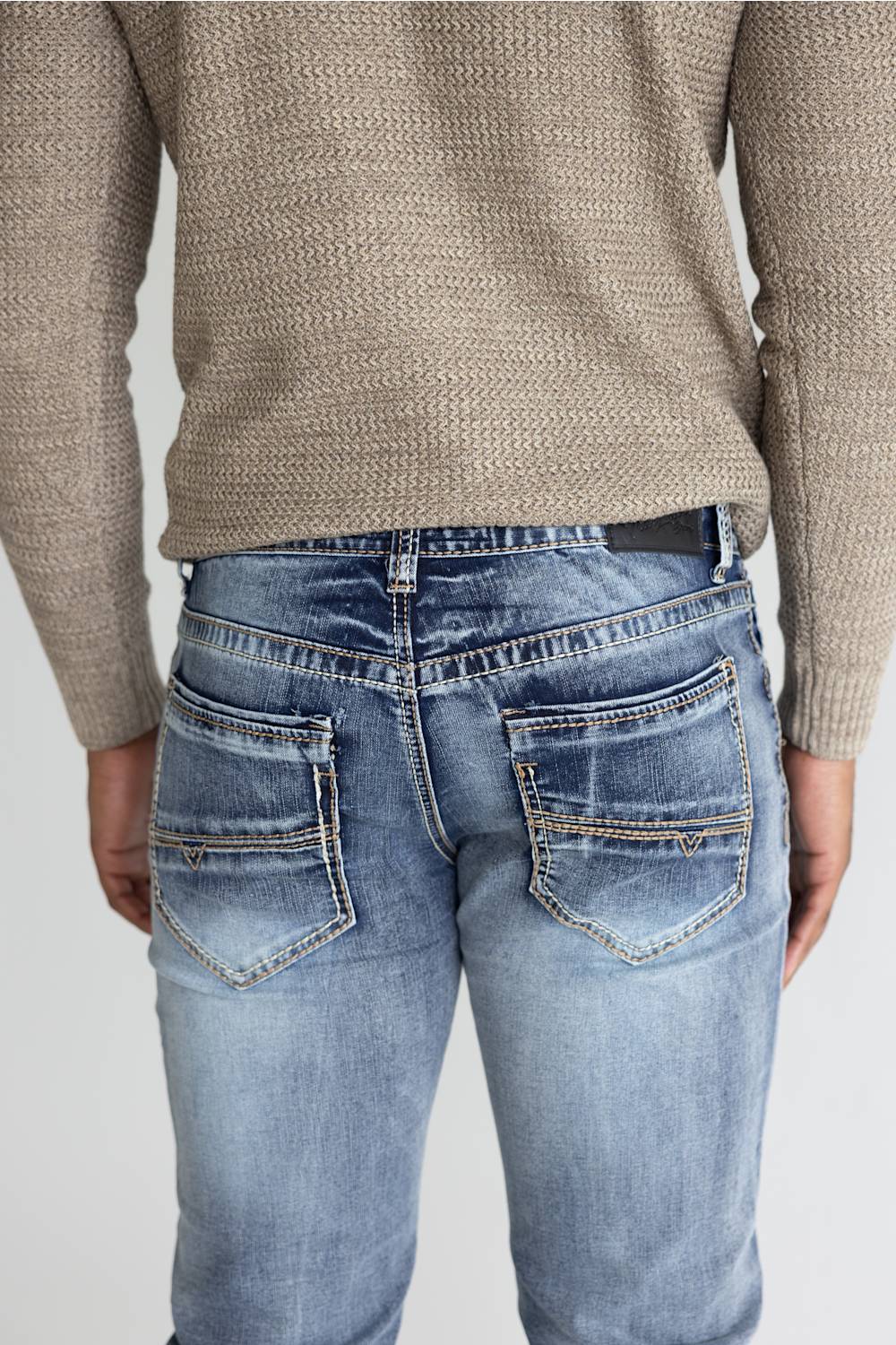 Rear view of a person wearing light blue denim jeans with a textured beige knit sweater, showing the back pockets and waistband details against a light gray background.