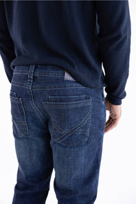Rear view of a person wearing dark blue denim jeans and a dark navy long-sleeve top against a plain white background.