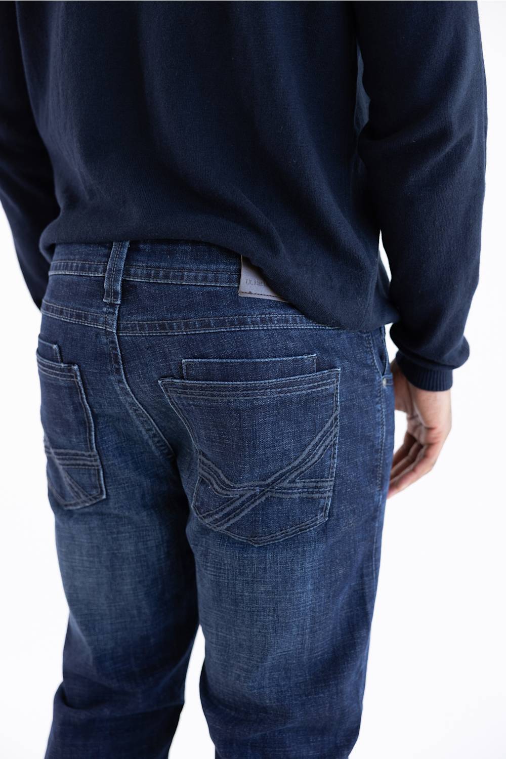 Rear view of a person wearing dark blue denim jeans and a dark navy long-sleeve top against a plain white background.