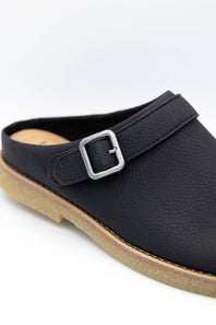 A close-up of a black pebbled leather clog shoe with a silver metal buckle strap and a tan sole, shown on a white background.