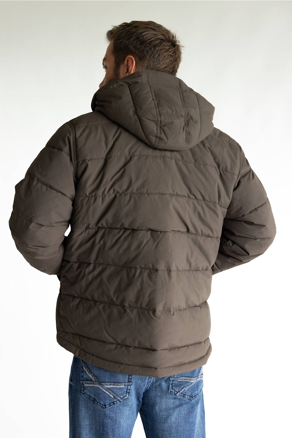 A man viewed from behind wearing a dark brown puffer jacket with a hood and blue jeans, set against a plain light gray background.