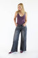 A woman modeling a sleeveless purple tank top and wide-leg gray jeans with burgundy sneakers, standing against a plain white studio background.