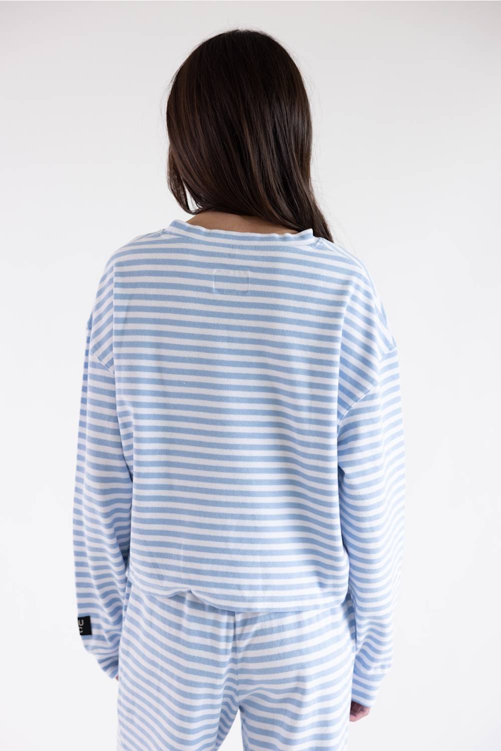 A person viewed from the back wearing a light blue and white striped long-sleeve top and matching striped pants against a plain light gray studio background.