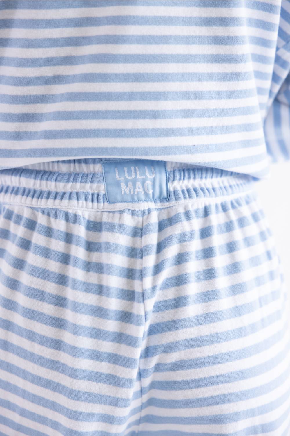Close-up of a blue and white striped children's pajama set, showing the elastic waistband with a light blue fabric label that reads 'LULU MAG'.