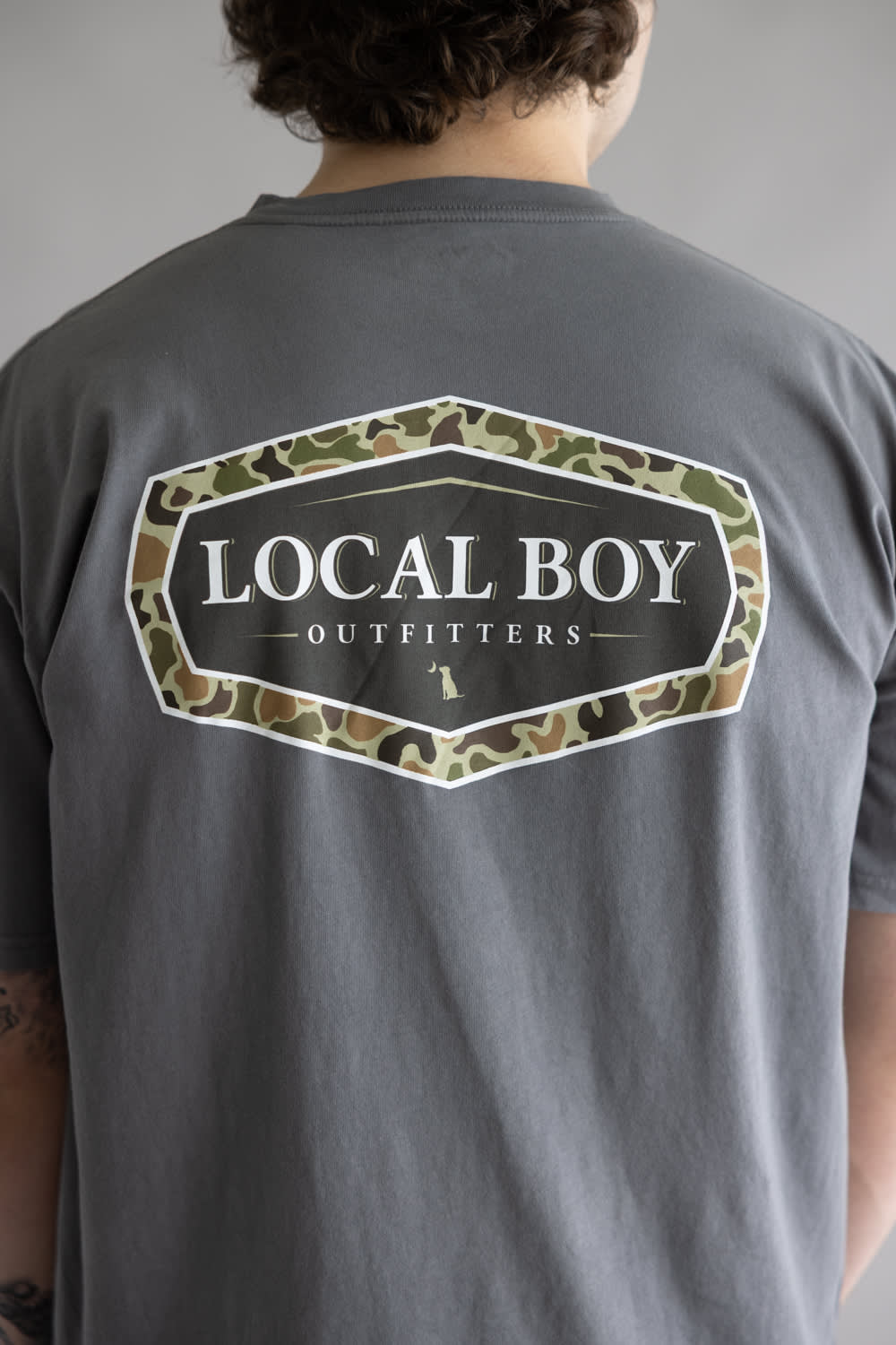 Local Boy Vintage Emblem T-Shirt for Men in Grey; Person wearing a gray t-shirt with 'Local Boy Outfitters' logo on the back.