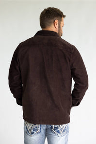 A man viewed from behind wearing a dark brown corduroy jacket and light blue jeans with western-style embroidery on the back pockets, set against a plain light gray background.