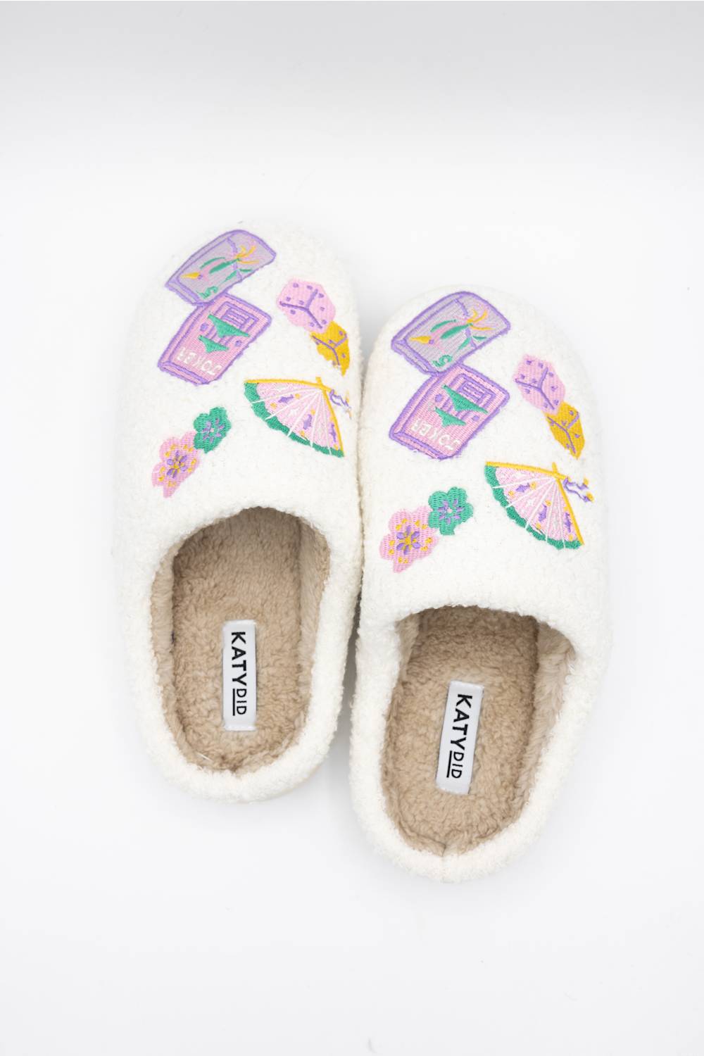 A pair of white fuzzy slip-on slippers with colorful embroidered patterns of majong and fans. The brand name 'KATYDID' is visible on the insole of each slipper, set against a clean white background.