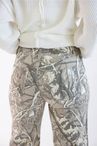 Close-up back view of a person wearing camouflage pants and a cream ribbed sweater against a plain light background.
