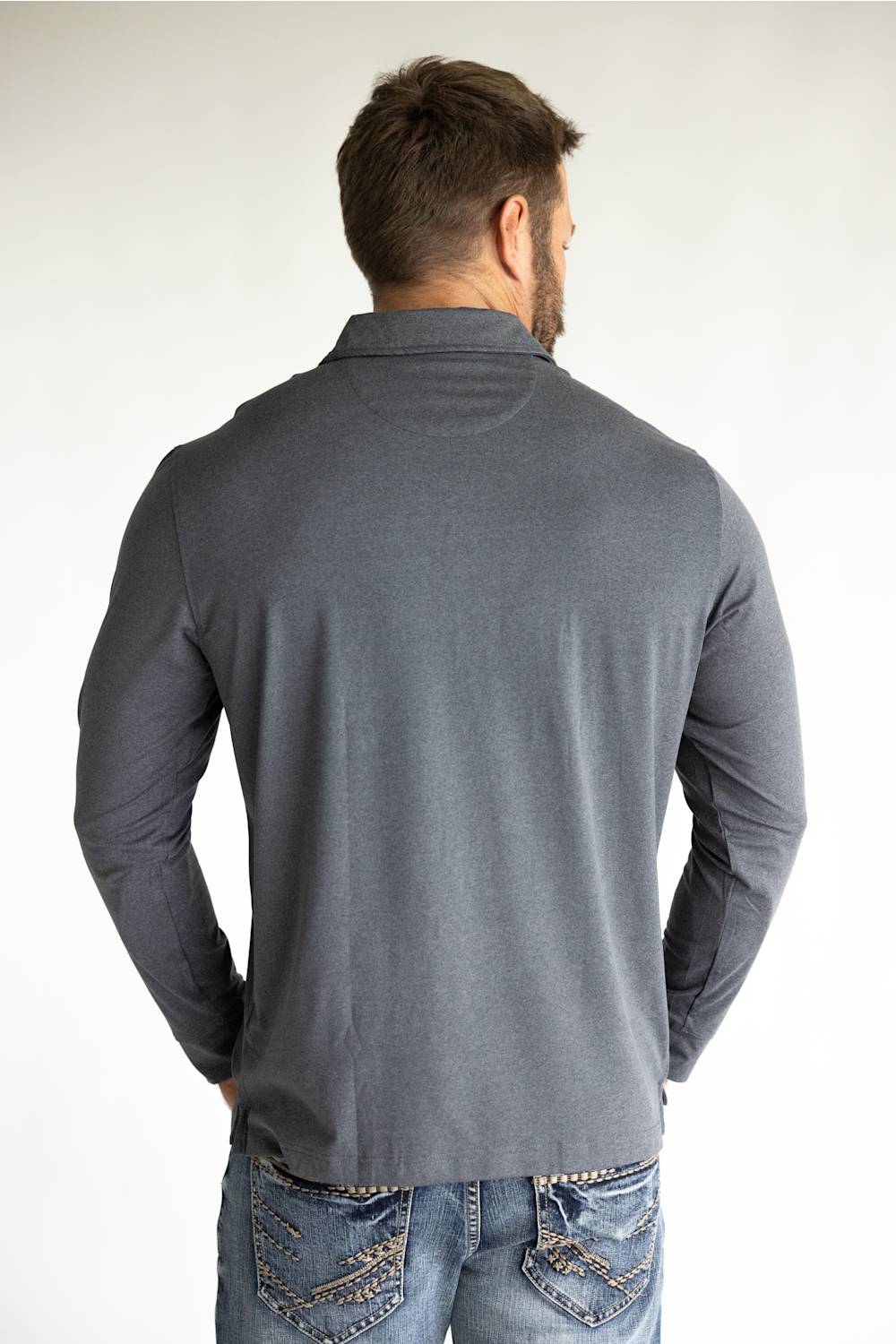 A man viewed from behind wearing a dark gray long-sleeve mock neck shirt and blue jeans with decorative stitching on the back pockets, against a plain white background.