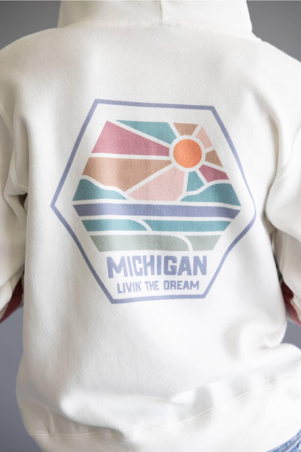 Close-up of the back of a white hoodie featuring a large hexagonal graphic with a retro sunset landscape and the text 'MICHIGAN' and 'LIVIN THE DREAM'.