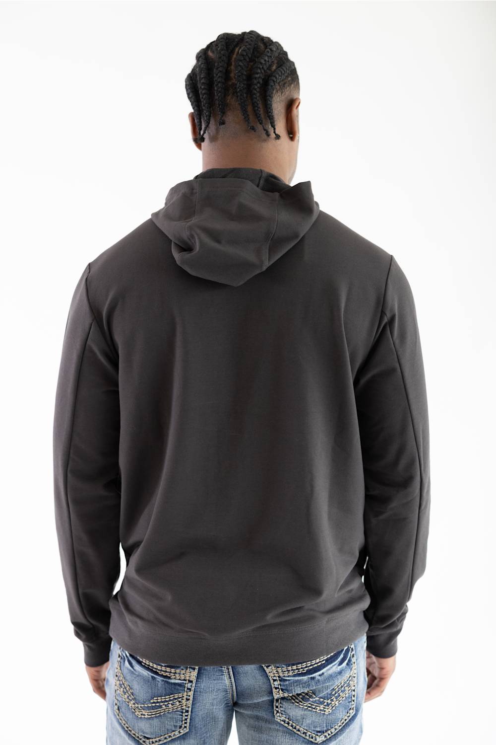 Back view of a model wearing a dark raven black long-sleeve hooded sweatshirt with the hood down, paired with light-wash blue jeans featuring white contrast stitching.