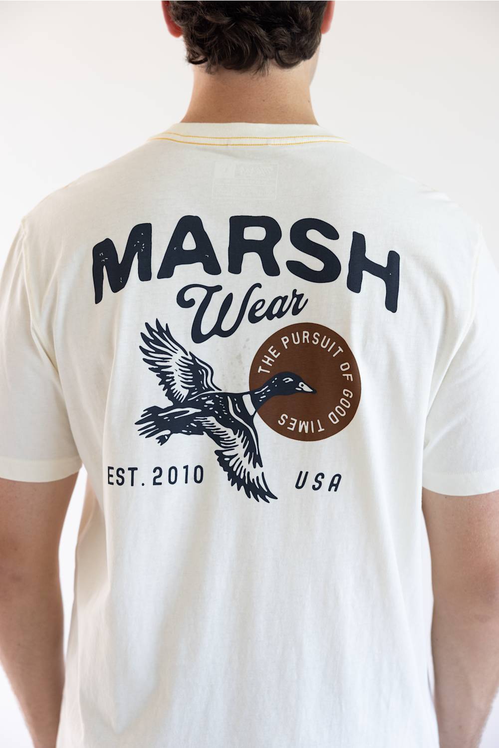 A man viewed from behind wearing a white t-shirt with a large back graphic that reads 'MARSH Wear' and features a duck and duck hunter illustration.