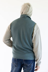A person shown from the back wearing a sleeveless ribbed knit vest over a light beige hoodie and blue jeans, against a plain white studio background.