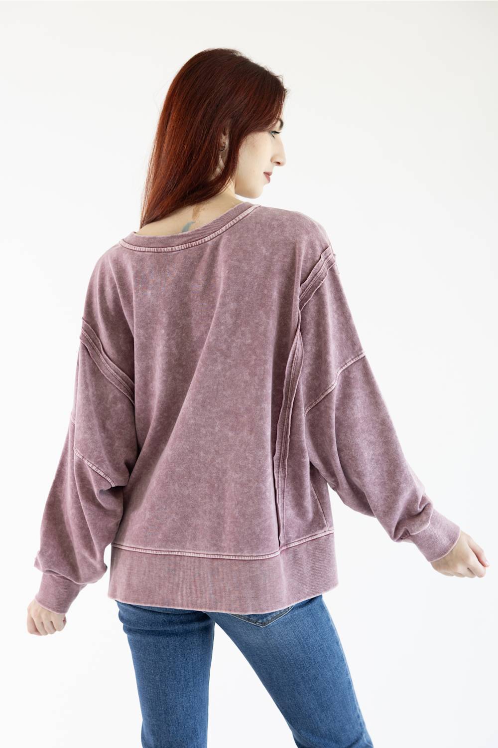 A woman wearing a washed mauve-purple long-sleeve sweatshirt and blue jeans, shown from the back against a plain white background.