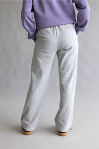 A person shown from the back wearing light heather gray wide-leg sweatpants and a lavender sweatshirt, standing against a plain light gray studio background.
