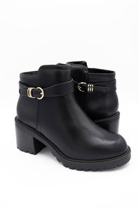 A pair of black leather ankle boots with chunky block heels, featuring a decorative strap with gold-tone buckles on the outer side and a side zipper, shown against a plain white background.