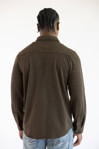 A man viewed from behind wearing a dark brown long-sleeve button-up shirt and light blue jeans against a plain white background.