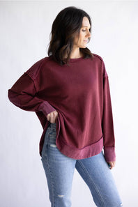 Woman wearing a burgundy oversized sweatshirt and light blue jeans on a white background
