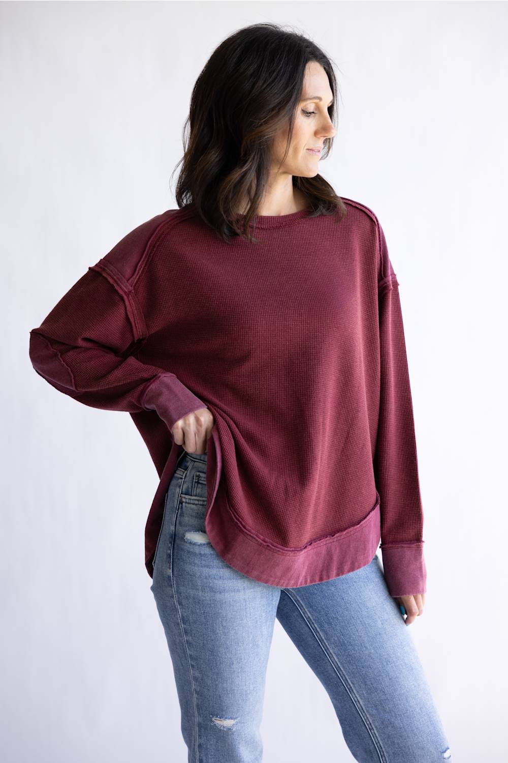 Woman wearing a burgundy oversized sweatshirt and light blue jeans on a white background