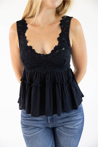 A woman wearing a black lace and tulle peplum top with blue jeans, shown from the neck down against a plain white background.