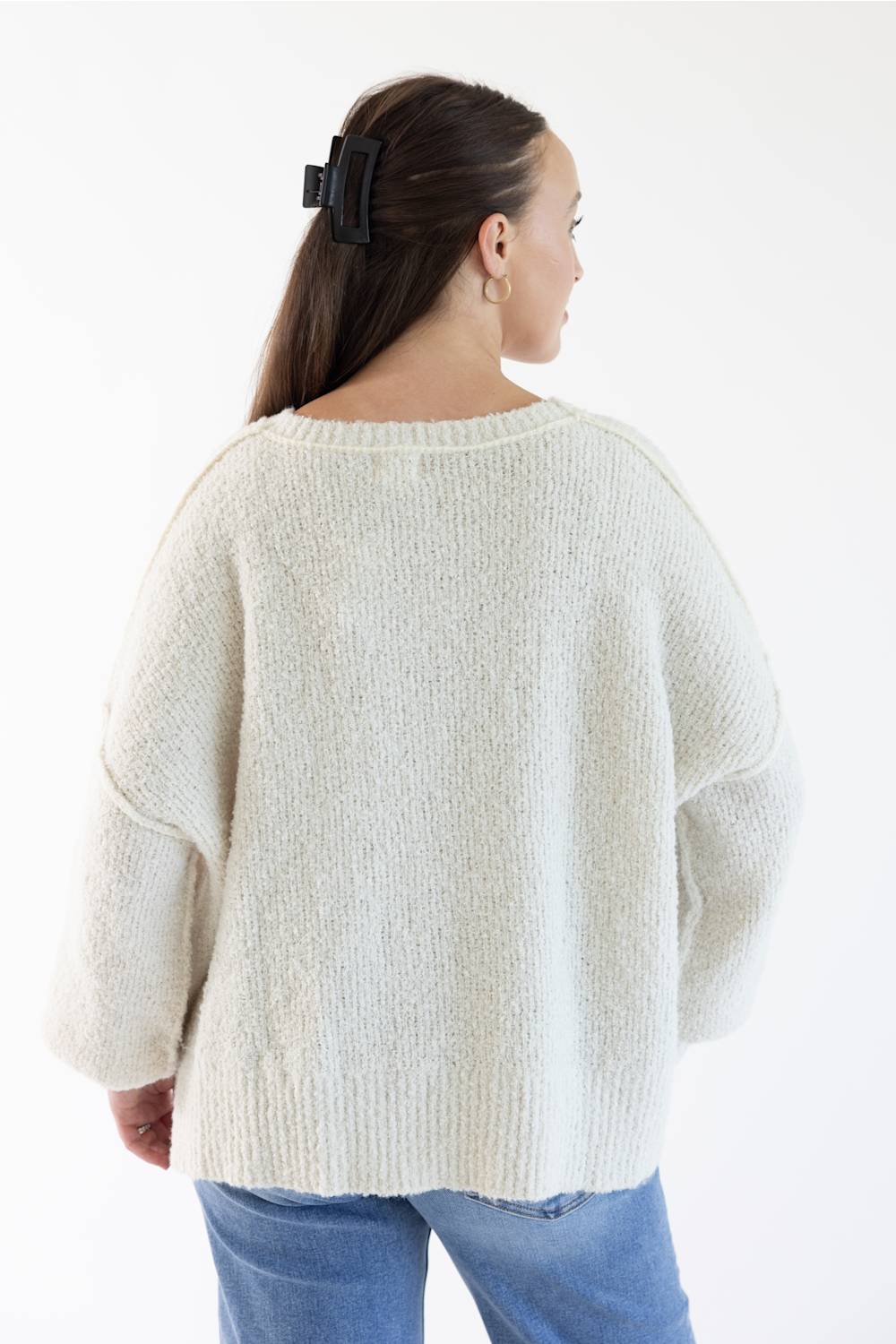 A woman shown from the back wearing a chunky knit cream-colored sweater and blue jeans against a plain white background.