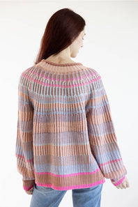 A woman viewed from the back wearing a chunky knit sweater with horizontal stripes in beige, light blue, and pink, paired with blue jeans against a plain white background.