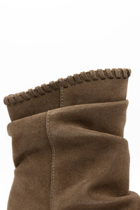 Close-up of a brown suede boot with a fringed edge and stitched details on a white background.