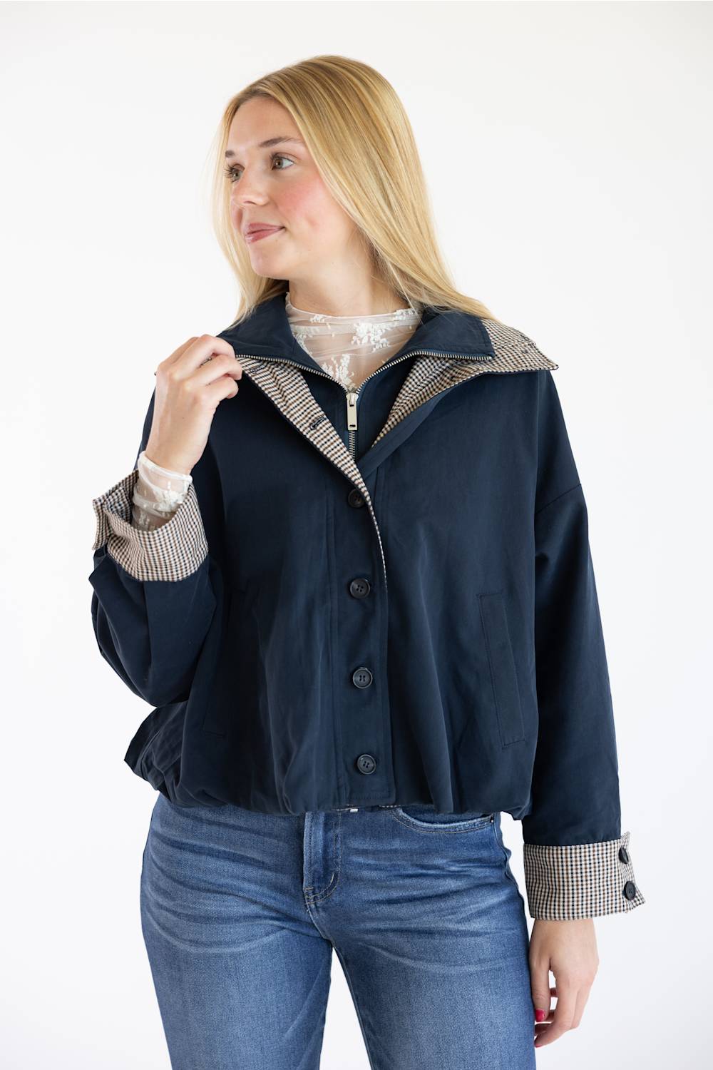 A woman wearing a navy blue cropped jacket with beige and black gingham patterned trim on the collar and cuffs, paired with blue jeans, against a plain white background.
