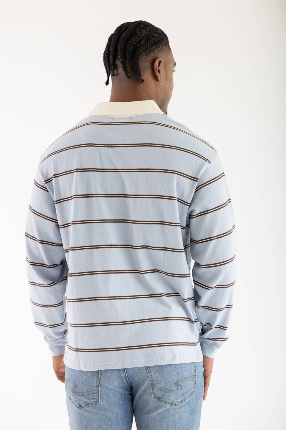 A man viewed from behind wearing a light blue long-sleeve striped shirt with brown horizontal stripes and a cream collar, paired with light blue jeans, against a plain white background.