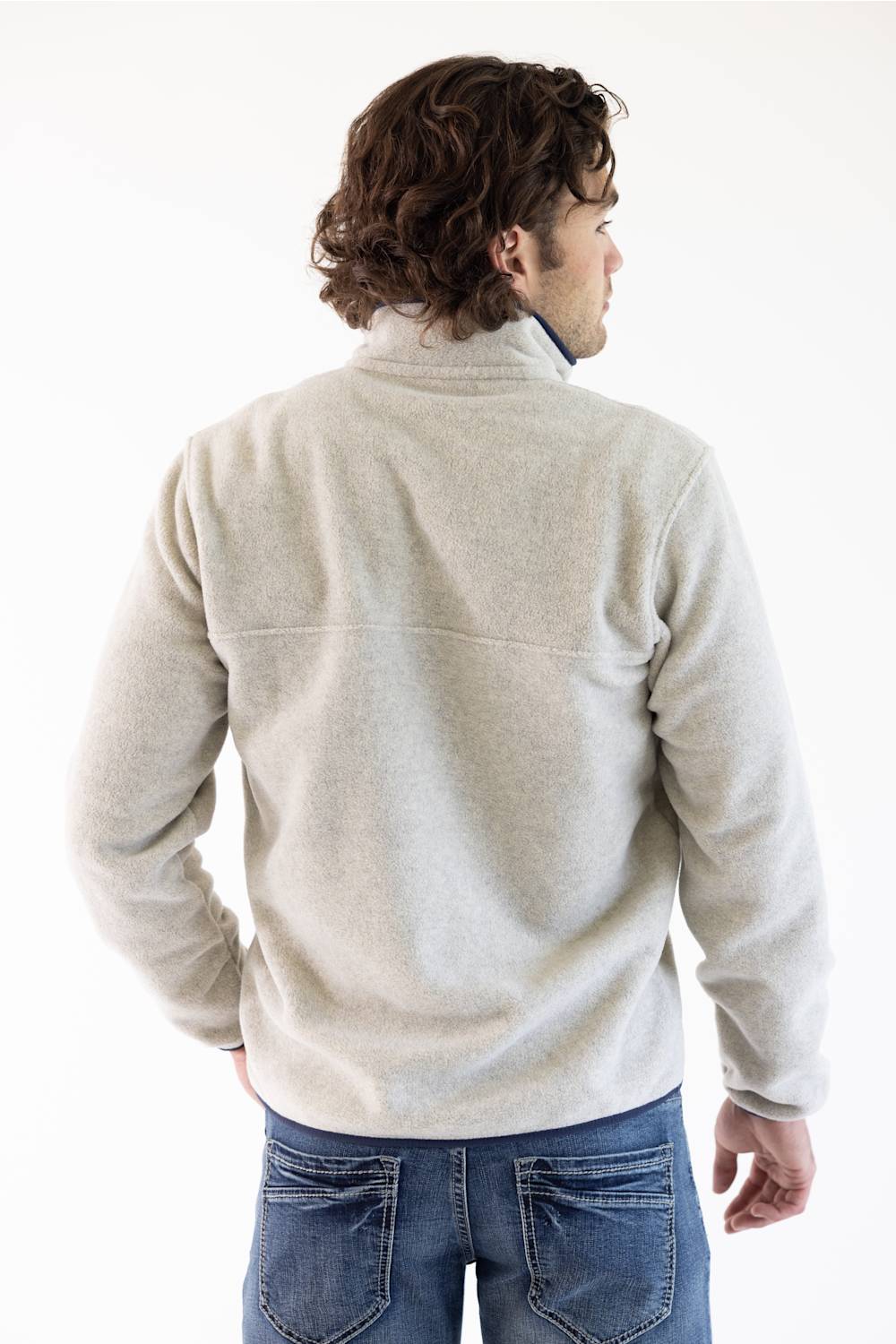 A man wearing a light beige fleece pullover sweater with a navy blue chest pocket and trim, paired with blue jeans, photographed against a plain white studio background.