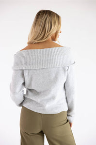 Back view of a blonde model wearing the Pink Rose heather grey off-the-shoulder knit sweater, showing the wide fold-over ribbed collar, long sleeves, and ribbed hem.