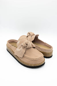 A single slip-on mule shoe in blush suede with a matching fabric bow on the vamp and a cork-textured midsole, shown against a plain white background.