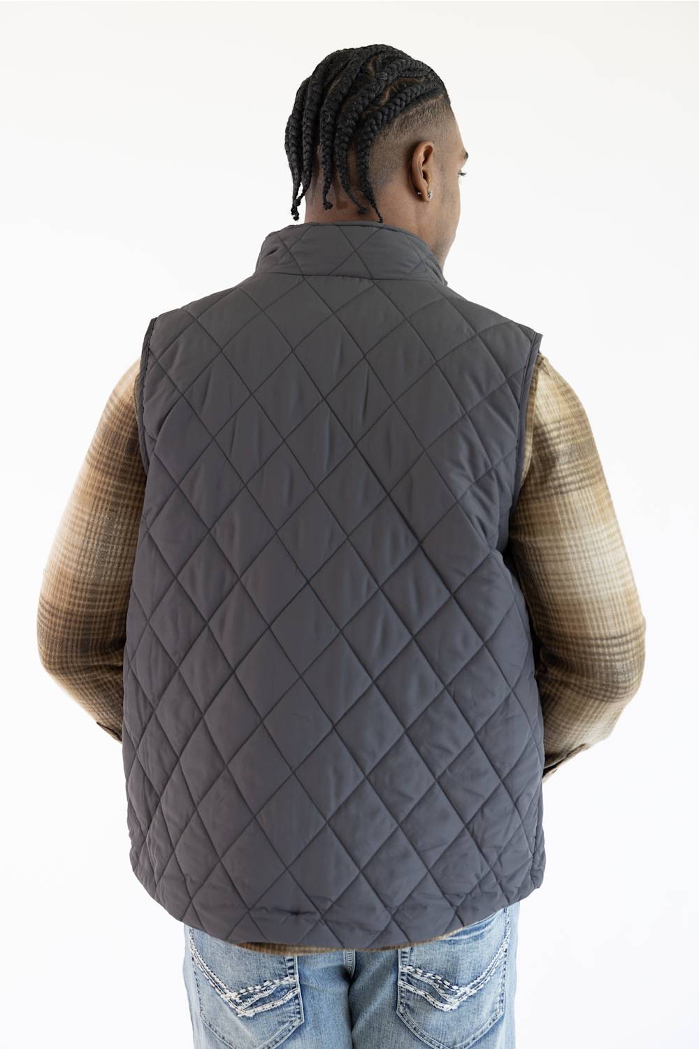 A man viewed from behind wearing a dark gray diamond-quilted puffer vest over a brown plaid shirt and blue jeans, against a plain white background.