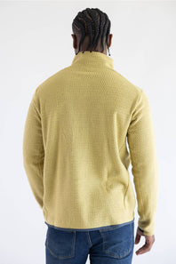 A man viewed from behind wearing a textured yellow quarter-zip fleece pullover and blue jeans, set against a plain white studio background.