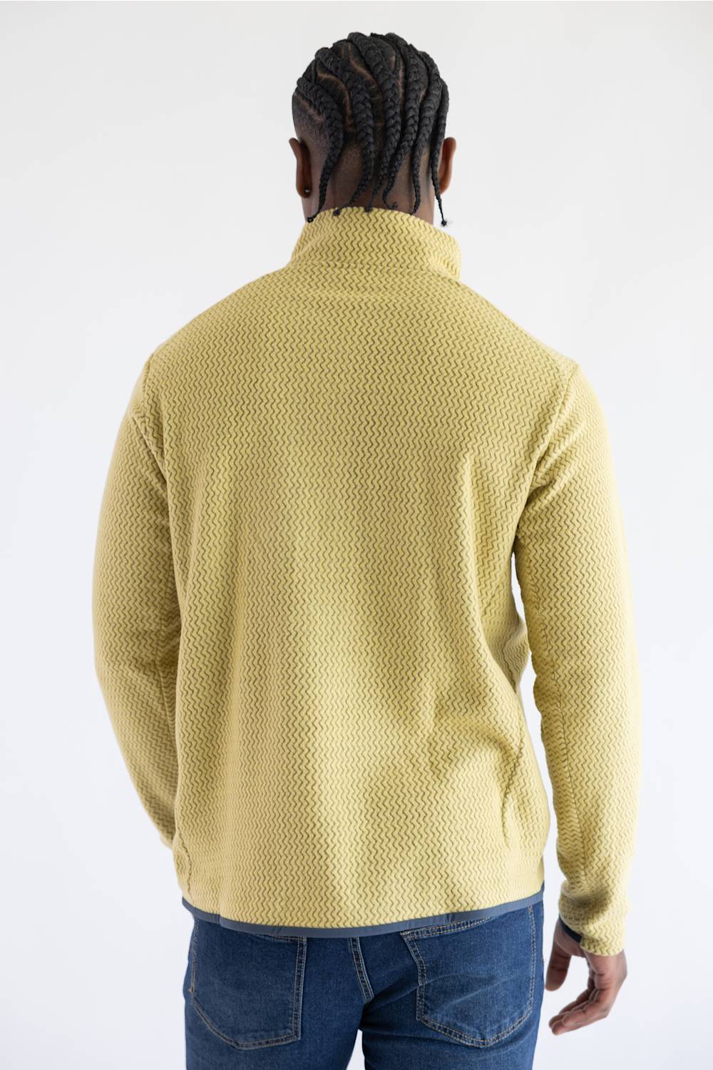 A man viewed from behind wearing a textured yellow quarter-zip fleece pullover and blue jeans, set against a plain white studio background.
