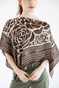 A woman wearing a sheer brown and beige patterned shawl draped over her shoulders, paired with olive green pants, against a plain white background.