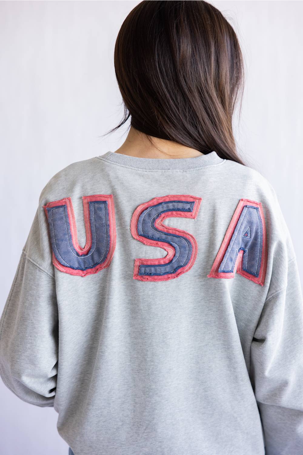 Flag USA Sweatshirt for Women in Grey; Person wearing a gray sweatshirt with 'USA' text on the back against a white background