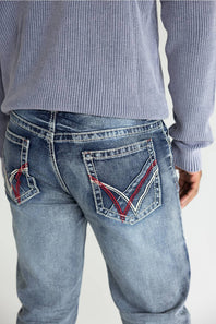 Close-up back view of a person wearing light-wash blue jeans with distinctive red and white contrast stitching on the back pockets, paired with a ribbed long-sleeve top against a plain light background.