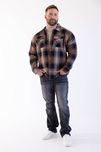 The model is standing facing forward with his hands in his pockets, wearing the sherpa-lined flannel shacket over a neutral crewneck shirt, paired with dark wash jeans and white sneakers.