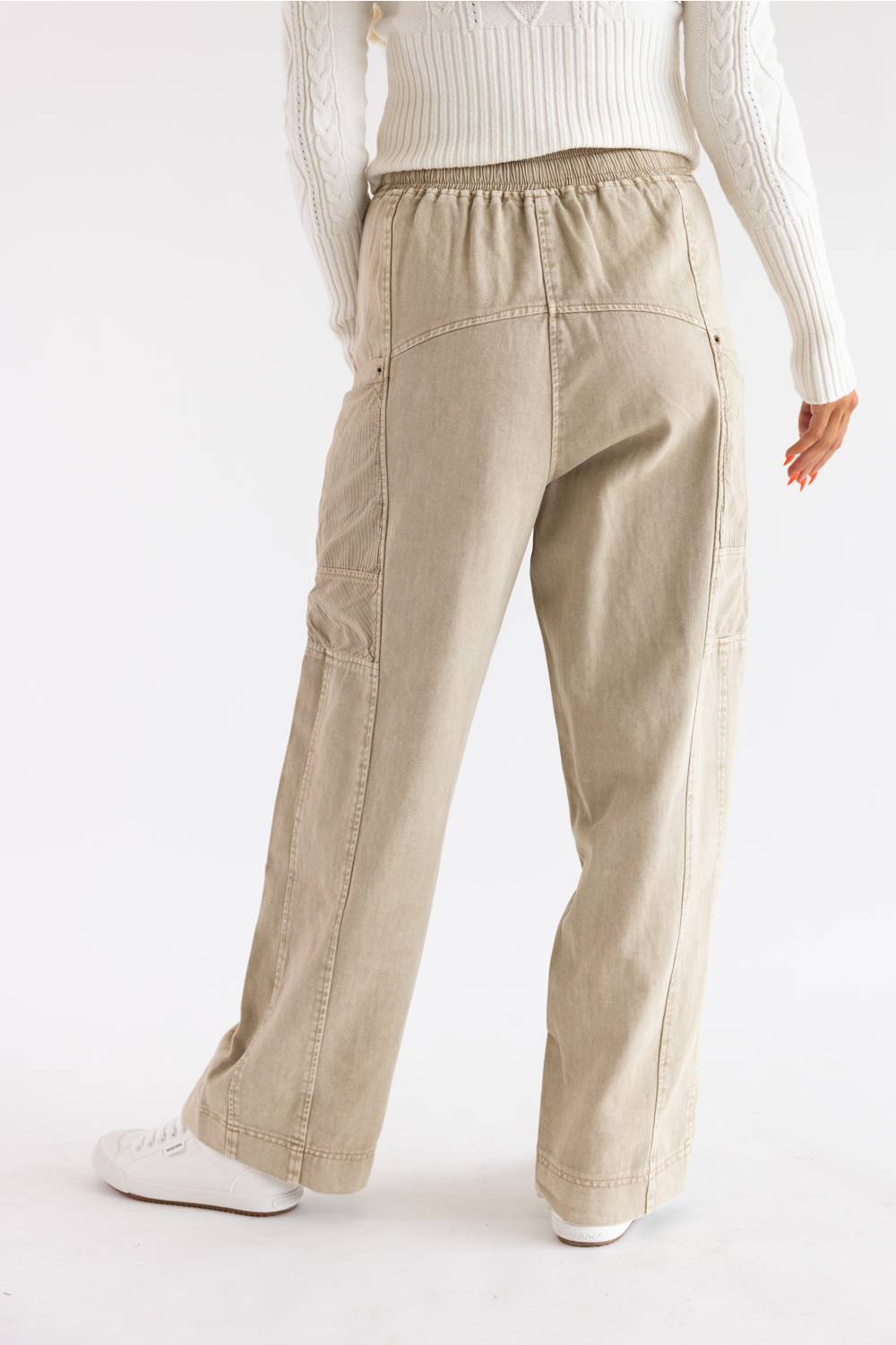 A person shown from the back wearing light beige wide-leg cargo pants, a white ribbed sweater, and white sneakers against a plain white studio background.